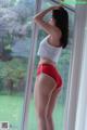 A woman in a white top and red shorts standing by a window.