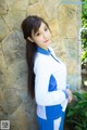 A woman in a blue and white uniform leaning against a stone wall.