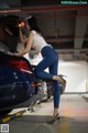 A woman leaning on the trunk of a blue car.