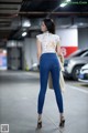 A woman in a white top and blue jeans standing in a parking garage.