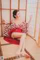 A woman in a red and white kimono sitting on a tatami mat.