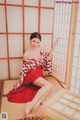 A woman in a red and white kimono sitting on a mat.