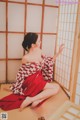 A woman in a red and white kimono sitting on the floor.