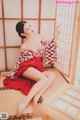 A woman in a red and white kimono sitting on a tatami mat.