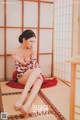 A woman in a red and white kimono sitting on a tatami mat.