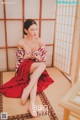 A woman in a red and white kimono sitting on a tatami mat.