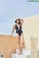 A woman in a black swimsuit leaning against a wall.