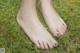 A woman's bare feet with purple nail polish on the grass.