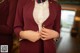 A woman in a maroon jacket and white shirt is adjusting her tie.