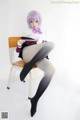 A woman sitting on a chair wearing black stockings and a purple wig.