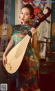 A woman in a floral dress holding a musical instrument.