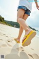 A woman walking on a sandy beach wearing yellow flip flops.