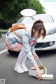 A woman in a school uniform crouching down next to a car.