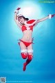 A woman in a red bikini and santa claus outfit jumping in the air.