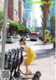 A woman in a yellow dress riding a scooter down a sidewalk.