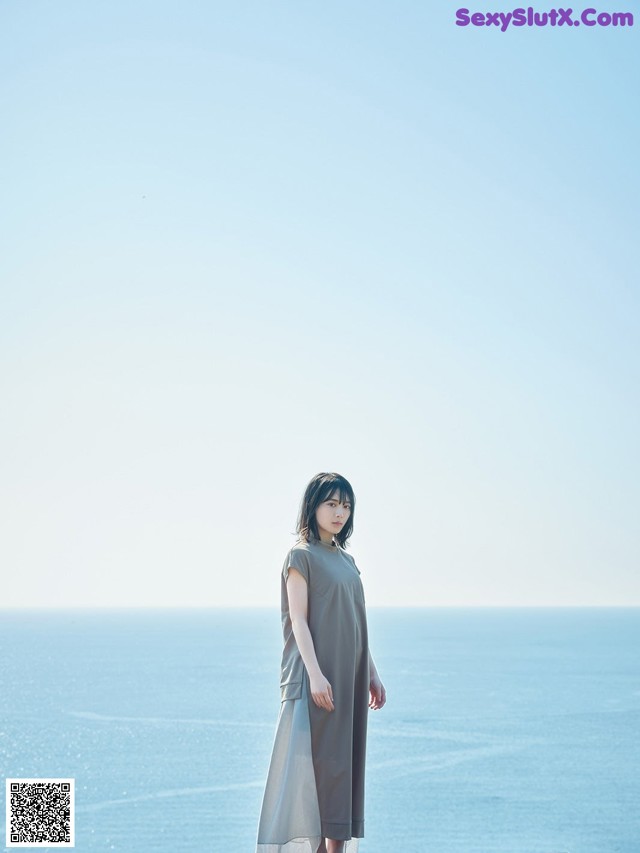 A woman standing on top of a cliff next to the ocean.