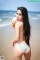 A woman in a bikini eating an ice cream cone on the beach.