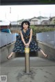 A woman in a blue dress sitting on a pole.