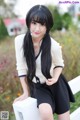 A woman with long black hair sitting on a white bench.