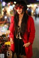 A woman in a red coat and sunglasses standing in front of a table of sunglasses.