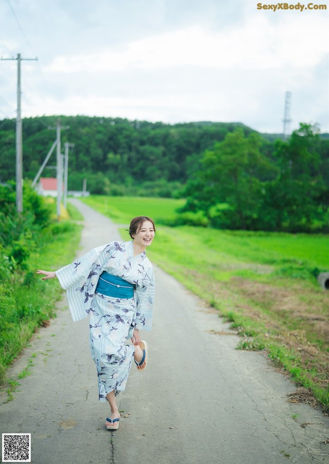 A woman in a blue and white kimono walking down a road.