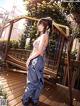 A woman in a bikini top and jeans standing on a wooden deck.