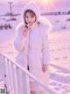 A young girl wearing a white coat and a white hat in the snow.