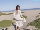 A woman in a white dress walking on a sandy beach.