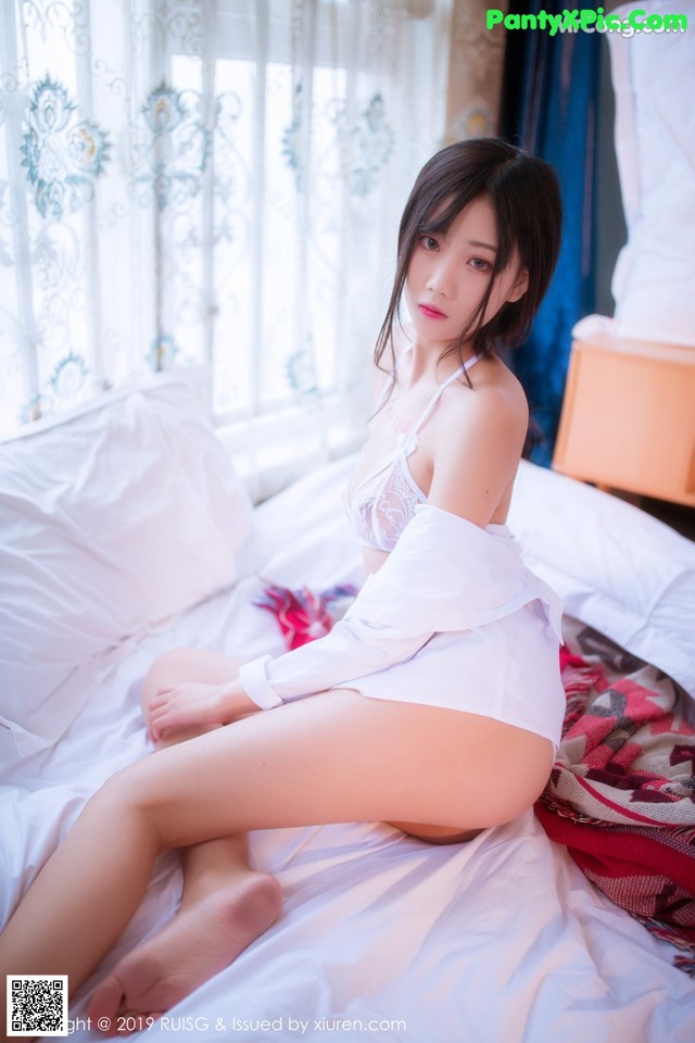 A woman sitting on a bed in a white lingerie.
