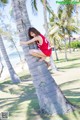 A woman in a red dress leaning against a palm tree.